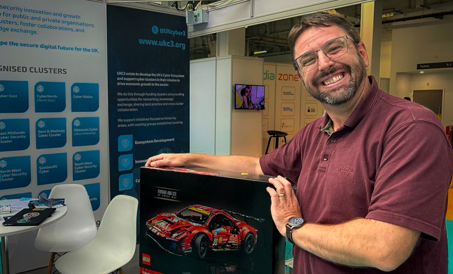 Pictured: Lego Ferrari Prize Winner, Sean Tonelli, Cyberpunk at BT Cables, holding their prize in front of the UKC3 stand at the International Cyber Expo